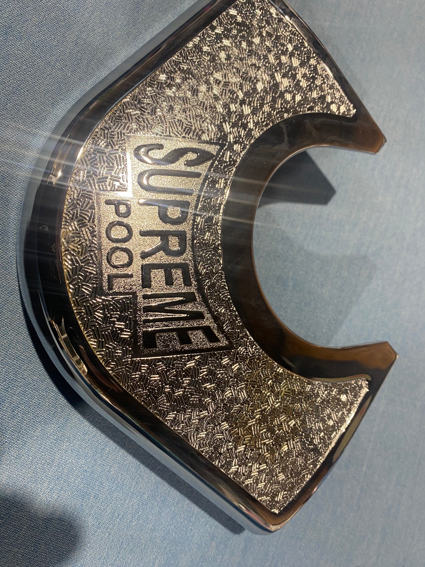 Close-up of SUPREME Winner chrome metal corner plate with engraved design.