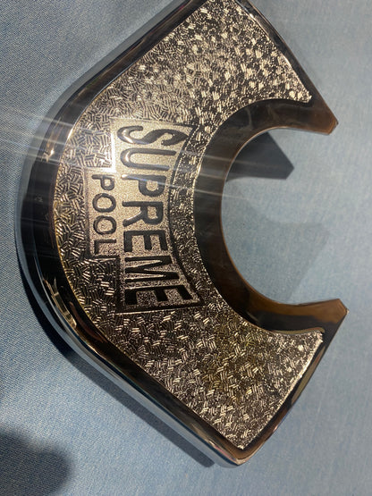 Close-up of SUPREME Winner chrome metal corner plate with engraved design.