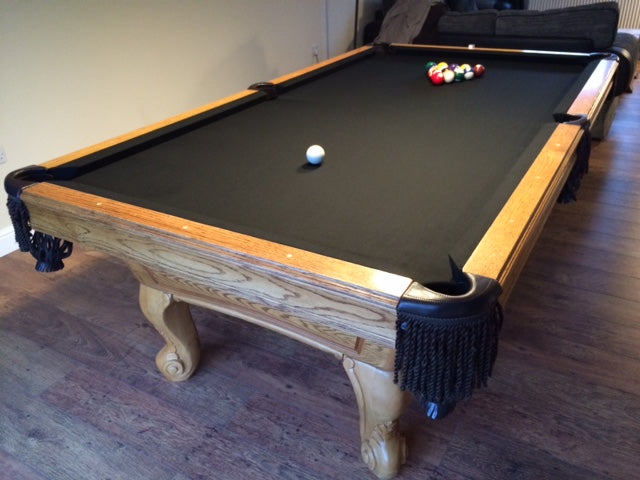 American pool table with black cloth and light wooden frame in a home setting.