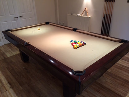 American pool table with beige cloth and wooden frame in a home setting.
