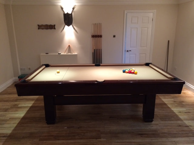 American pool table with beige cloth and dark wooden frame in a home setting.