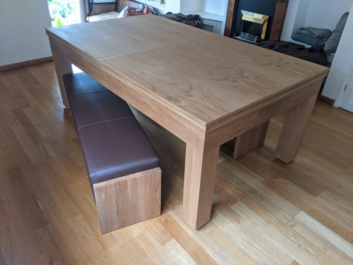 Oak dining pool table with benches in a bright living area.
