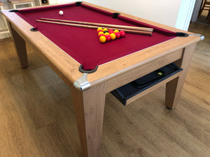 Supreme Oak Classic Diner pool table with red felt and cues on a wooden floor.