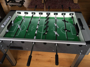 Side view of Roberto Sport football table with black handles and green playfield.