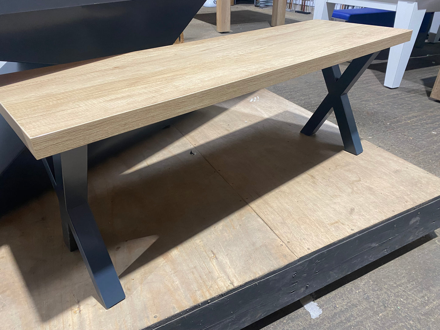 Cross leg pool dining table bench on a wooden platform in a showroom setting.