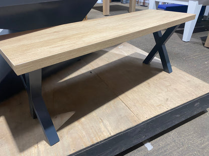 Cross leg pool dining table bench on a wooden platform in a showroom setting.
