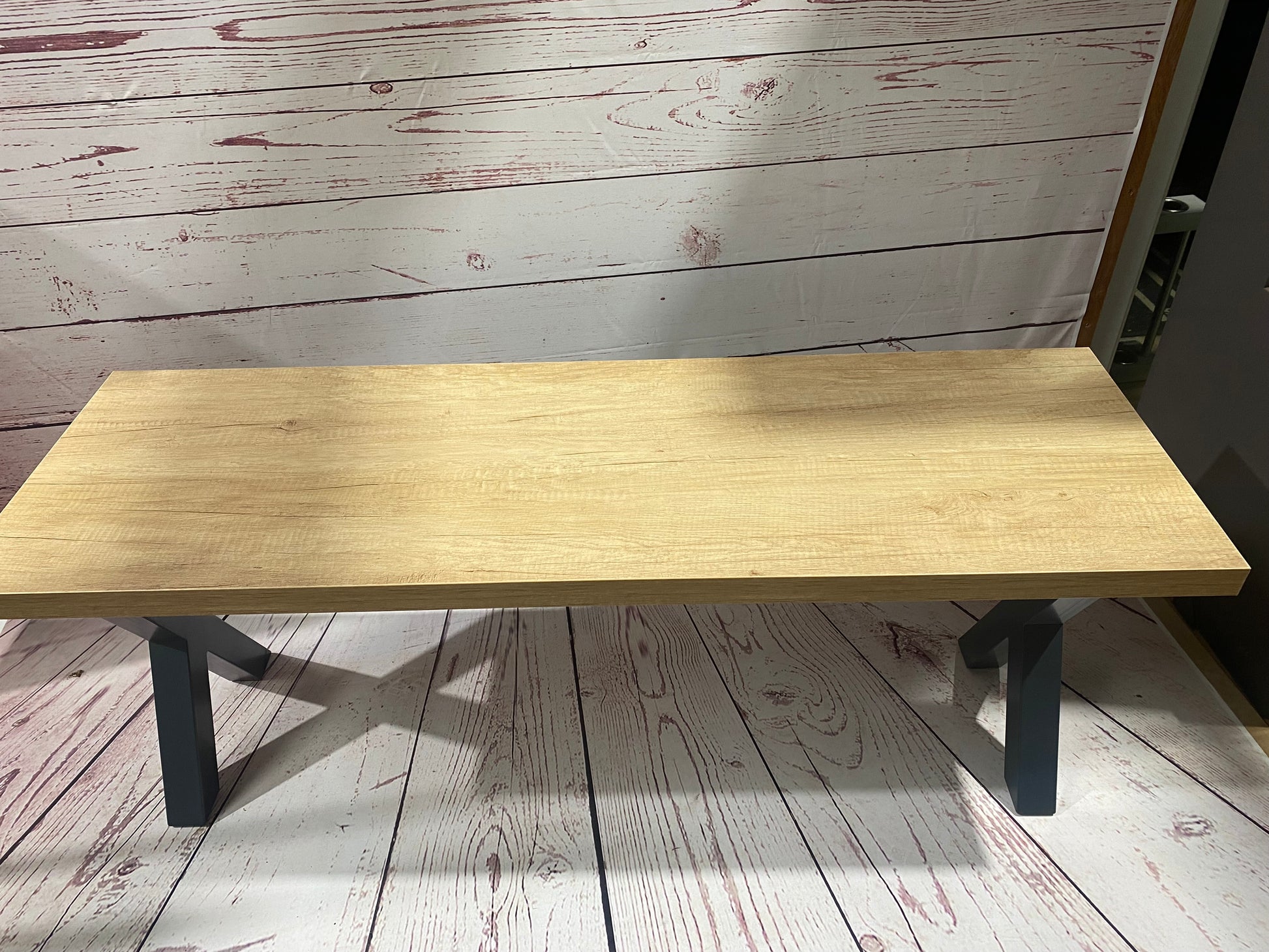 Cross leg pool dining table bench displayed on a wooden floor with rustic background.