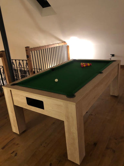 Classic oak pool table with green felt in a cozy loft space with warm lighting.