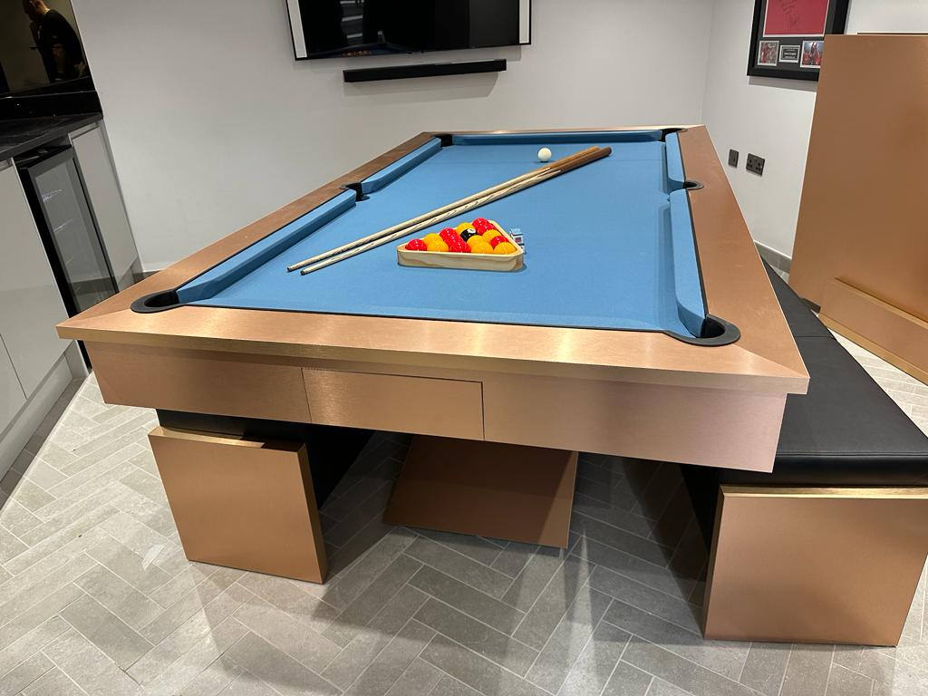 Elegant brushed copper pool diner table with blue felt and black seating.