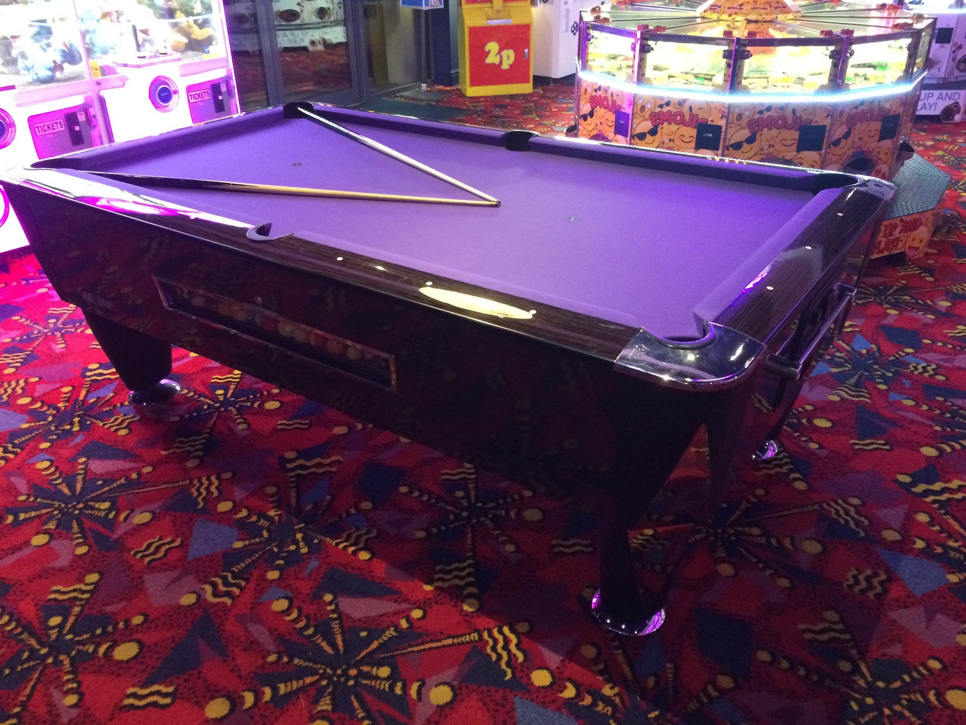 American pool table with purple cloth and black frame in an arcade setting.