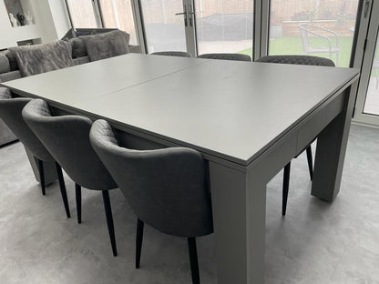 Modern Satin Grey Rosetta dining table with quilted grey chairs around it.