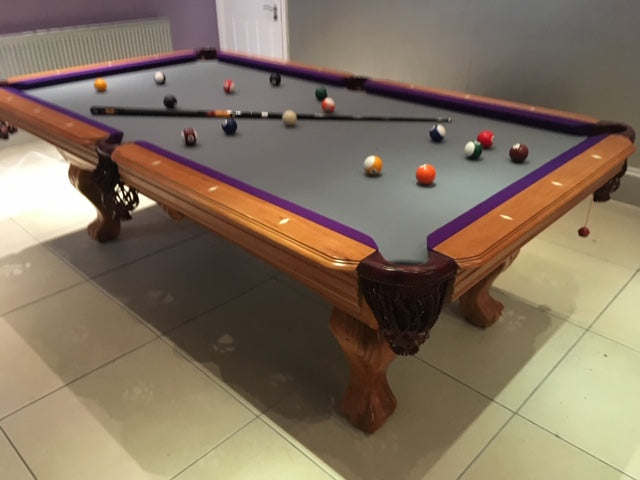 American pool table with gray cloth, purple trim, and ornate wooden legs.